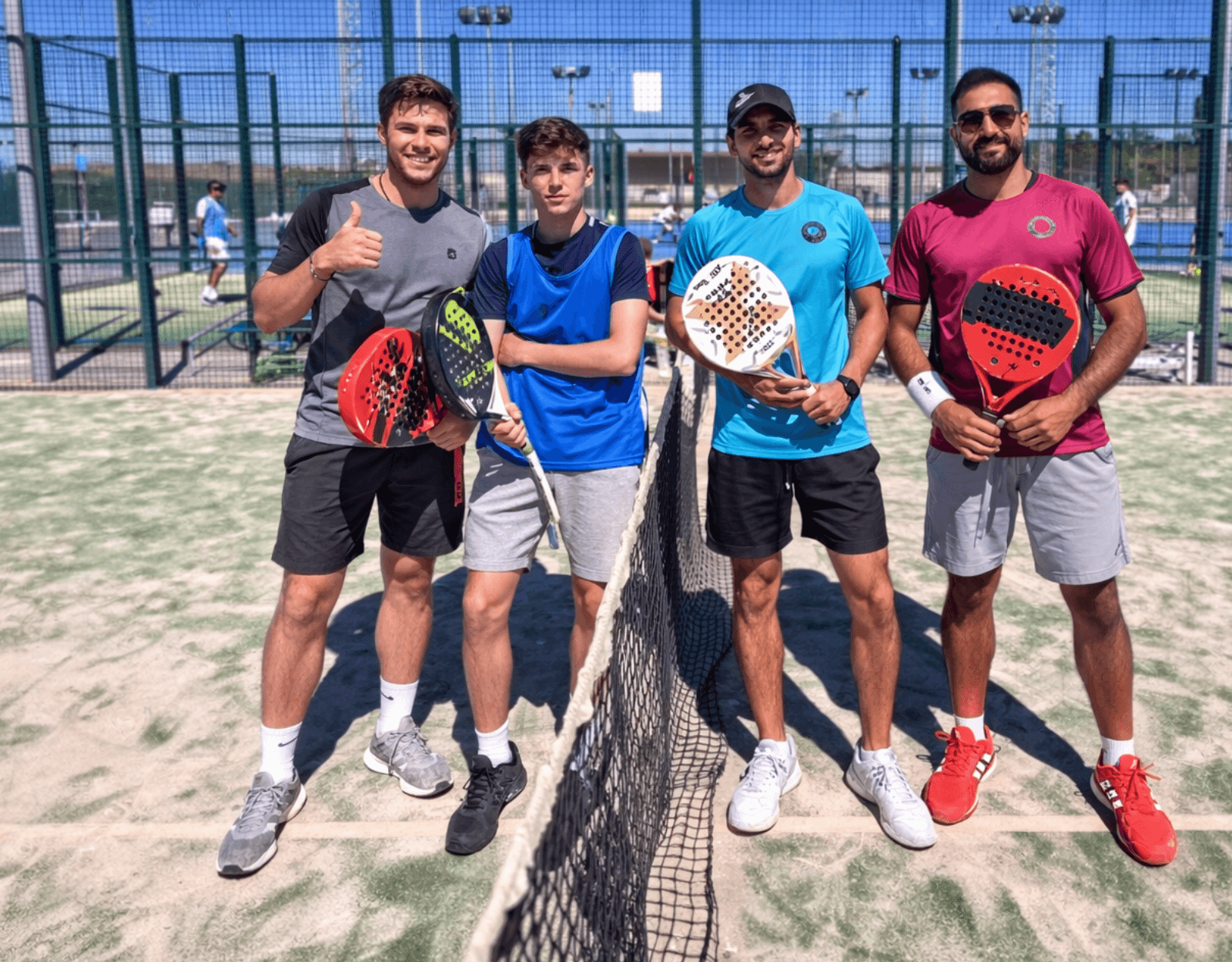 Four men in athletic wear pose with padel rackets on an outdoor court.